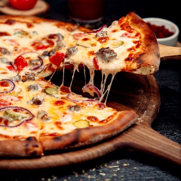 A slice of All Star Pizza Bar's pizza, topped with meat, onions, and pickles, being lifted with gooey cheese.
