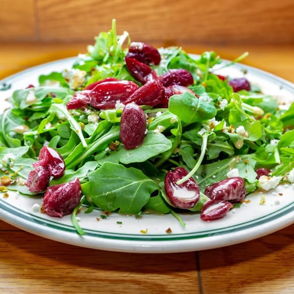 Arugula salad with red grapes, feta cheese, and dressing on a white plate with green stripes.