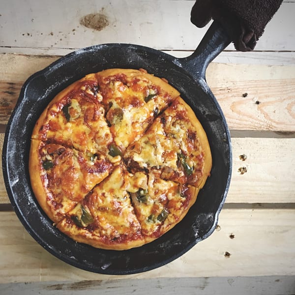 All Star Pizza Bar's deep-dish pizza, sliced in a cast iron pan on a rustic wooden table.