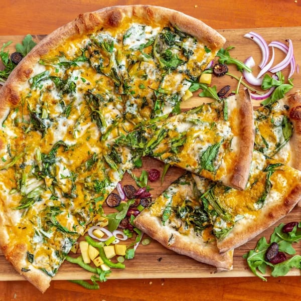 All Star Pizza Bar's white pizza with green vegetables and yellow sauce, sliced on a wooden board.